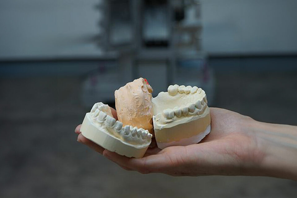 Plaster recycling with the jaw crusher type EB a hand holds old plaster casts from the dentist in front of the single-toggle crusher in the foreground
