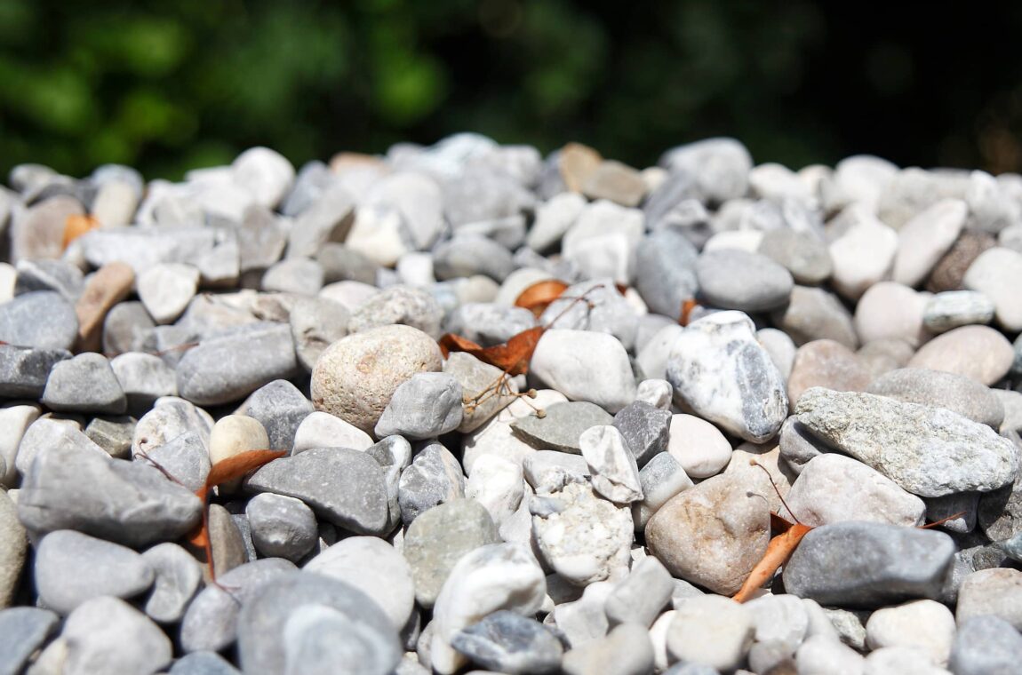 Gravel - stones of different sizes and colors in a pile, with a few wilted leaves in between